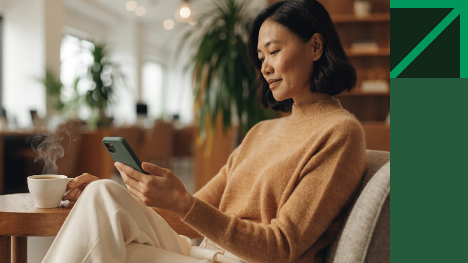 Frau am Schreibtisch überlegt am Smartphone, ob ETF vs Fonds die bessere Wahl ist