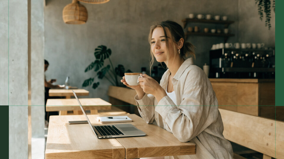 Woman with coffee and a laptop in a Bali café — how to invest in ETFs
